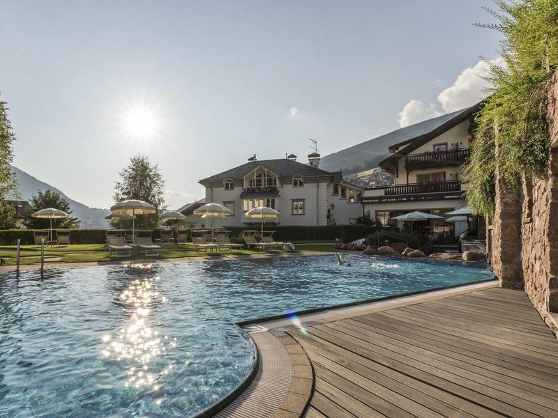 Outdoor pool in front of hotel with mountain view under sunny sky and wooden deck