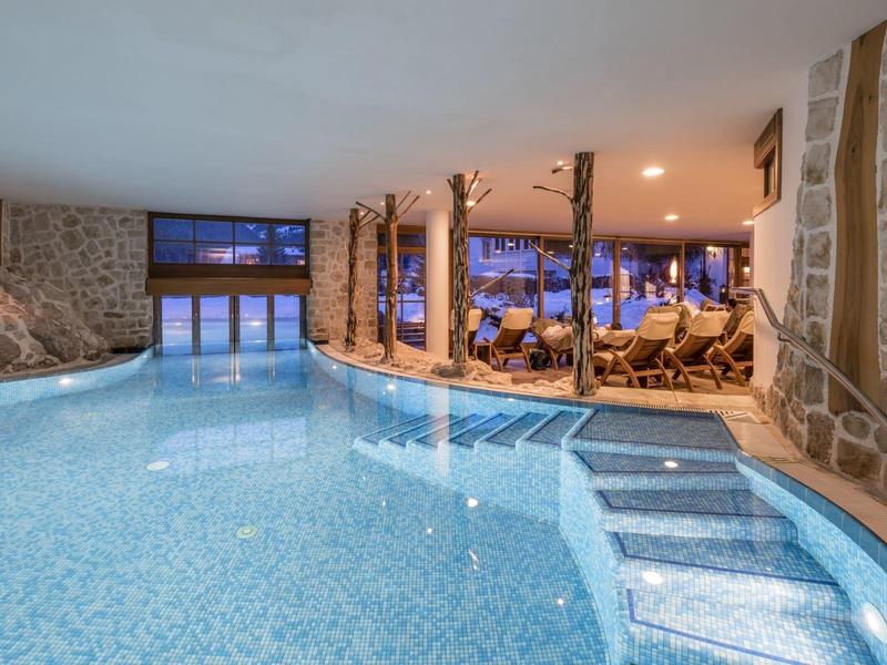 Modern indoor pool with seating areas and stone walls, illuminated in the evening.