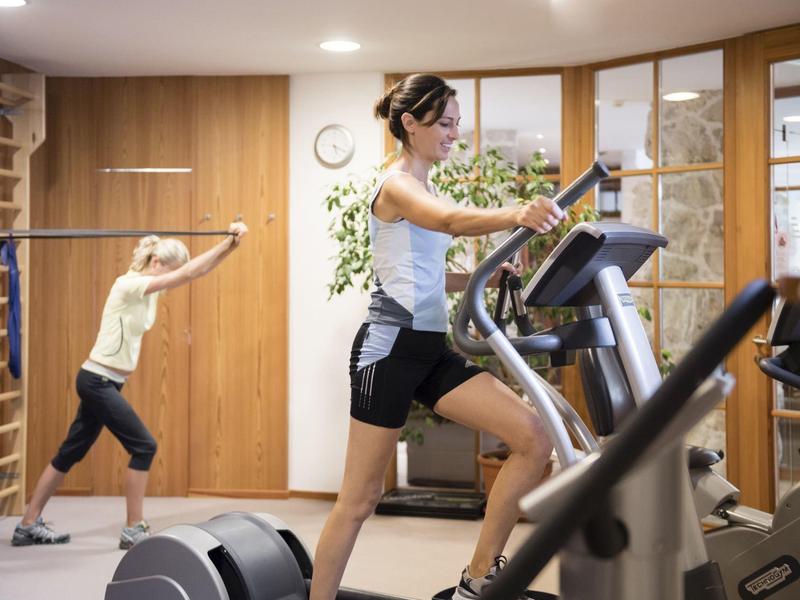 Two women exercising in a bright hotel gym with wooden paneling.