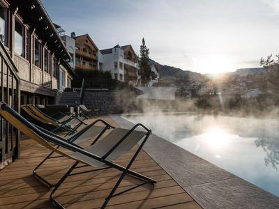 Leere Liegestühle neben einem dampfenden Pool vor Gebäuden bei Sonnenaufgang.