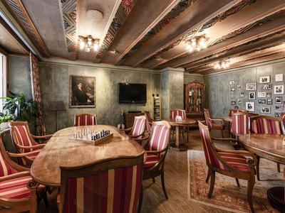 Gemütlicher Speisesaal mit Holzbalken, gemusterten Sesseln und rustikalen Holztischen.