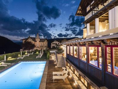 Außenbereich eines Hotels mit beleuchtetem Pool und Bergkulisse bei Dämmerung.