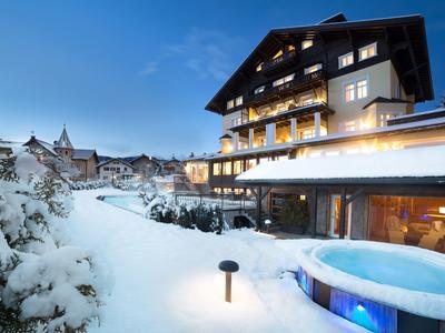 Hotel in paesaggio invernale innevato con vasca idromassaggio illuminata e montagna sullo sfondo al crepuscolo