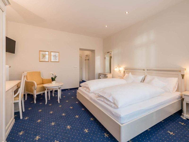 Camera d'hotel luminosa con letto grande, area salotto, scrivania e TV a muro.