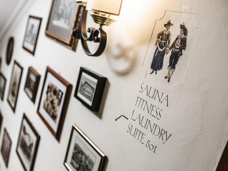 Corridoio d'hotel con lampade da parete vintage e quadri incorniciati accanto a un cartello di lavanderia.