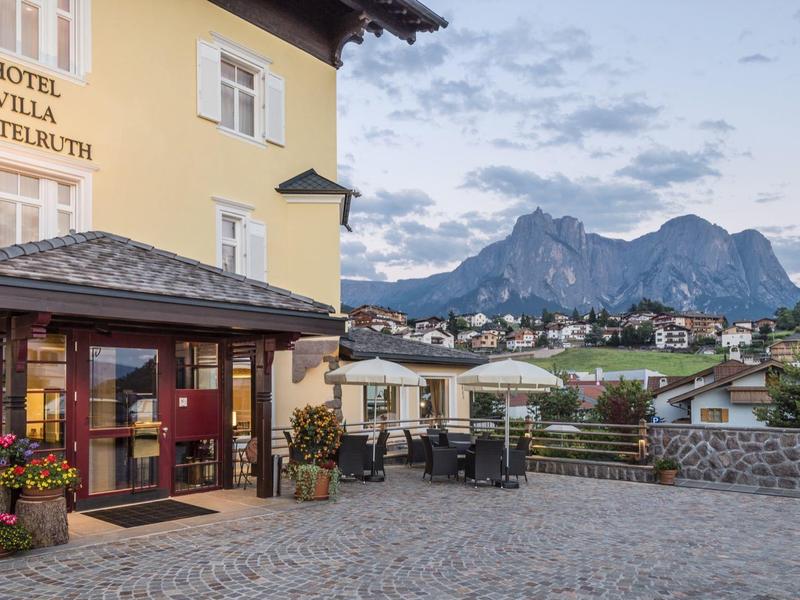 Hotel giallo con terrazza e vista sulle montagne al tramonto.