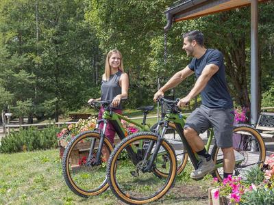 Due persone con biciclette si rilassano nel giardino davanti a una casa.