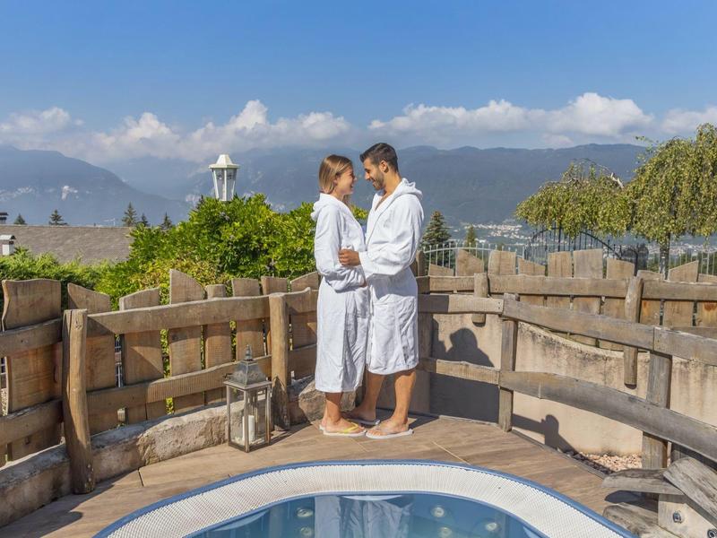 Pár v županech stojí na terase u bazénu s výhledem na hory