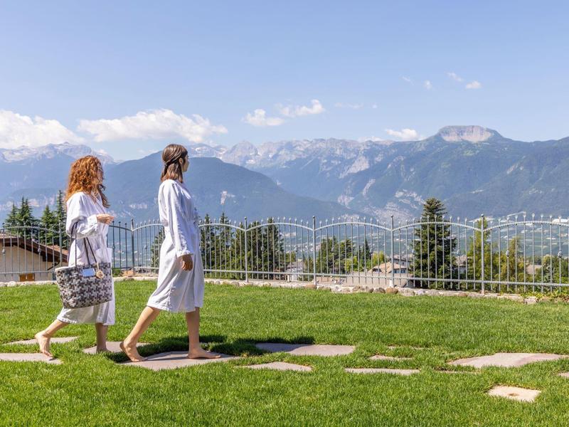 Dvě ženy v županech kráčí po zelené trávě s výhledem na hory.