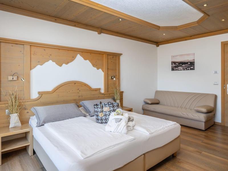 Světý hotelový pokoj s manželskou postelí, pohovkou, dřevěným nábytkem a dekorativním stropním prvkem.