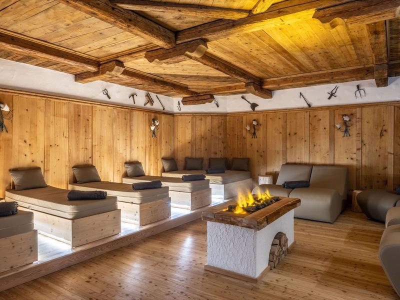 Pohodlná wellness místnost s dřevěným obložením, lehátky a centrálním krbem.