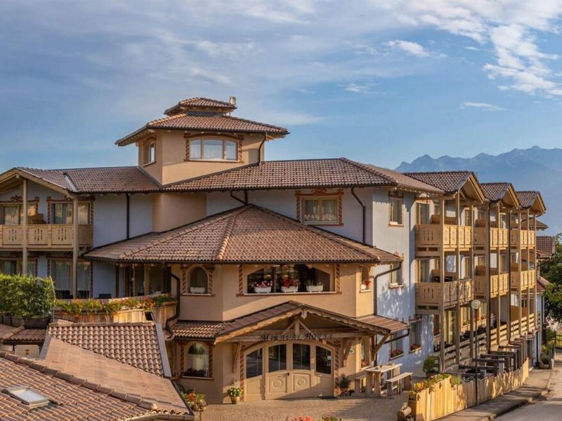 Velká hotelová budova s hnědými střechami před horami a modrou oblohou.