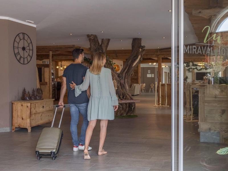 Pár vstupuje do hotelové lobby s kufrem, rustikální interiér.