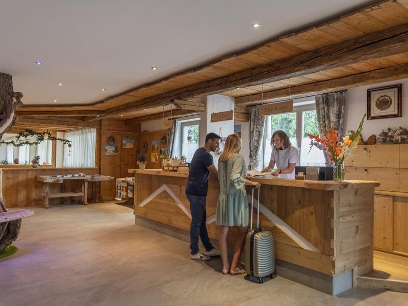 Hotelová recepce s hosty a recepčními v útulné místnosti s dřevěnými a přírodními prvky.