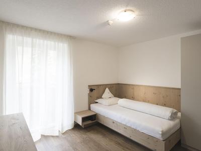 Brightly furnished hotel room with single bed, small nightstand, and large window with curtains.