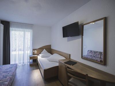 Modern hotel room with single bed, desk, TV, and window with curtains.