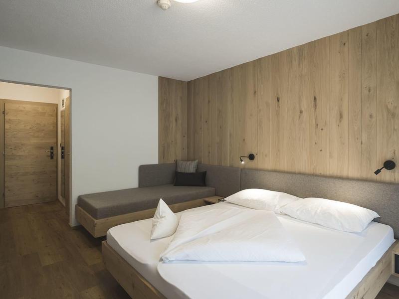 Modernes Hotelzimmer mit Holzwand, großem Bett, Einzelbett und schlichtem Design in neutralen Farben.