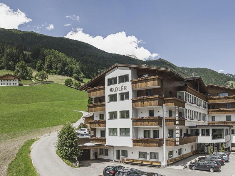 Großes Hotelgebäude mit mehreren Stockwerken, umgeben von grünen Bergen und Parkplatz mit Autos.