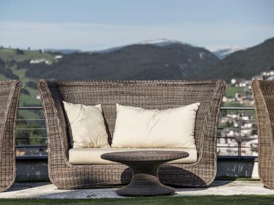 Outdoor-Sitzgruppe aus Rattan mit Polsterkissen auf Terrasse vor Berglandschaft bei klarem Himmel.