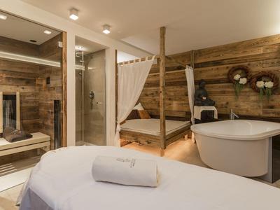 Modernes Badezimmer mit freistehender Badewanne, Holzwänden und gemütlichem Bett im Hintergrund.