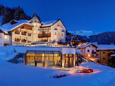 Winterliche Berglandschaft mit schneebedeckten Häusern und beleuchtetem Gebäude bei Abenddämmerung.