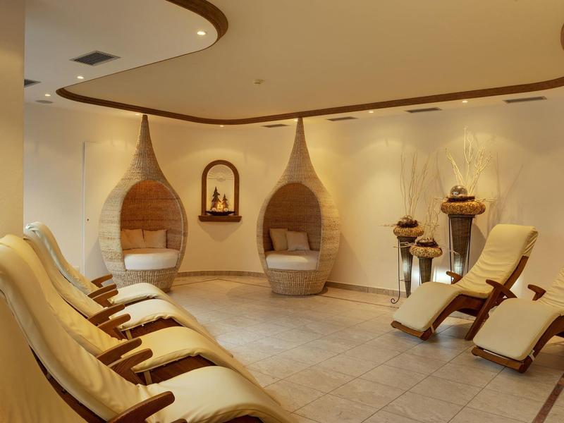 Gemütlicher Wellnessraum mit hängenden Korbsesseln und beige Liegen in warmem Licht.