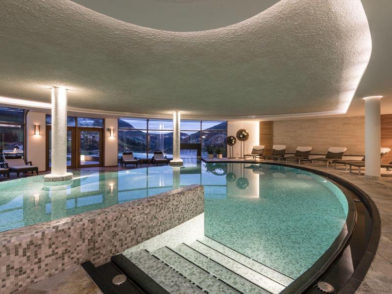 Moderner Indoor-Pool mit geschwungener Form, beleuchteter Decke und Relaxliegen am Rand.
