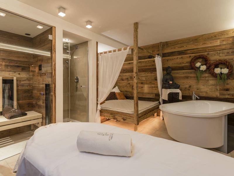 Modernes Badezimmer mit freistehender Badewanne, Holzwänden und gemütlichem Bett im Hintergrund.