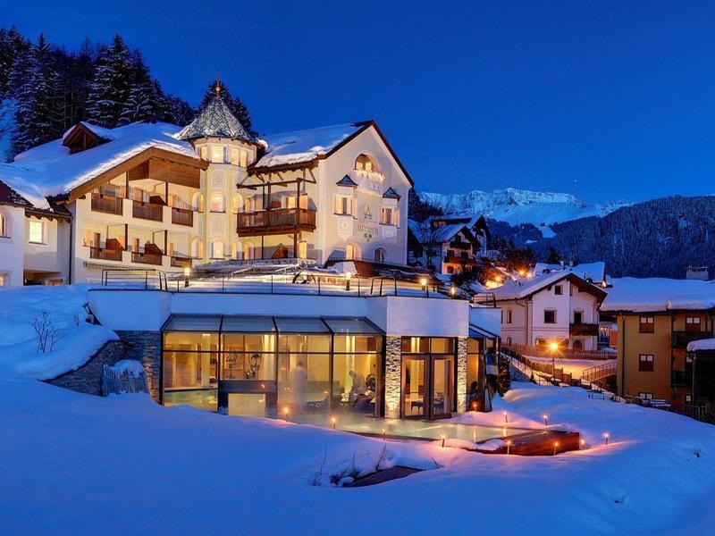 Winterliche Berglandschaft mit schneebedeckten Häusern und beleuchtetem Gebäude bei Abenddämmerung.