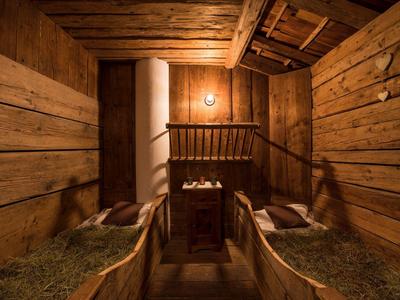 Rustikaler Pferdestall mit Holzwänden, eingestreutem Stroh und zentralem Holztisch unter warmer Beleuchtung.