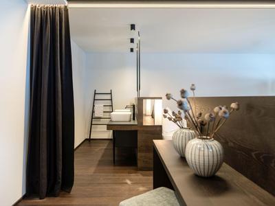 Habitación de hotel moderna con cortinas oscuras, muebles de madera y jarrón decorativo sobre la mesa.
