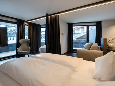 Habitación de hotel moderna con cama doble, sillones y grandes ventanas con vistas a edificios nevados.