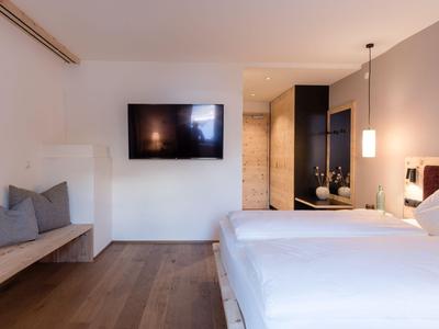 Habitación de hotel moderna con cama grande, televisor de pared y banco con cojines.