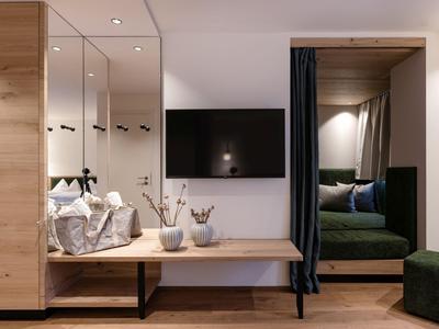 Habitación de hotel moderna con decoración en madera, espejo de pared, TV y zona de estar acogedora con cortina.