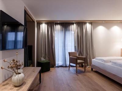 Habitación de hotel moderna con cama, televisor y balcón con cortinas.