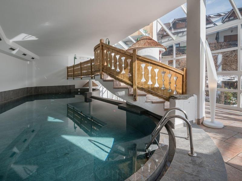 Innenpool mit Holzbrücke, Glasdach und großer Glasfront, helle Atmosphäre, moderne Ausstattung.