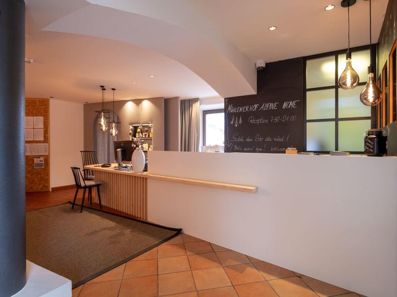 Der helle Empfangsbereich mit Tresen, Hockern und Wandtafel in modernen, warmen Farben.