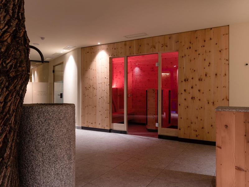 Moderner Saunabereich mit Holzverkleidung, geschlossener Glastüren und roter Beleuchtung innen.
