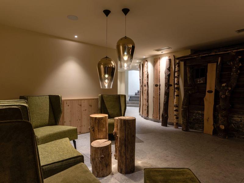 Gemütlicher Raum mit grünen Sesseln, hölzernen Hockern und warmem Licht in gedämpfter Atmosphäre.