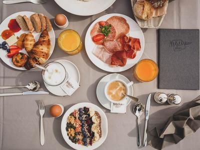 Frühstückstisch mit Brötchen, Aufschnitt, Müsli, Eiern, Kaffee und Orangensaft in stillem Grau.