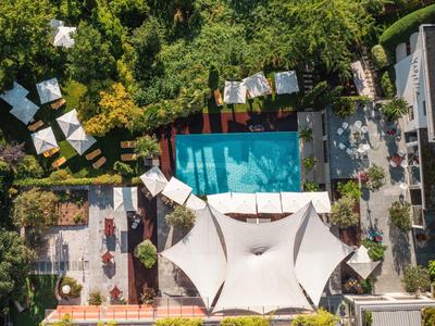 Luftaufnahme eines Pools mit mehreren weißen Sonnenschirmen und viel grüner Vegetation.