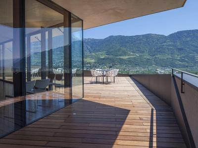 Große Holzterrasse mit Glasschiebetüren, modernem Geländer und Bergblick im Hintergrund.