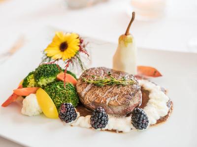 Ein kunstvoll angerichtetes Gericht mit gebratenem Fleisch, Beeren, Gemüse und Blume auf weißem Teller.