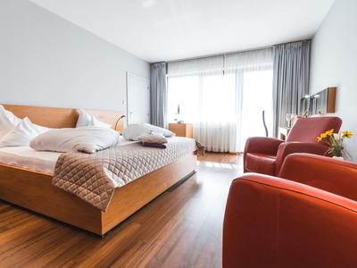 Helles Schlafzimmer mit Holzboden, zwei roten Sesseln und großem Doppelbett mit weißer Bettwäsche.