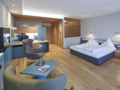 Moderner Hotelraum mit Doppelbett, Sitzecke, Holzboden und heller, harmonischer Einrichtung.