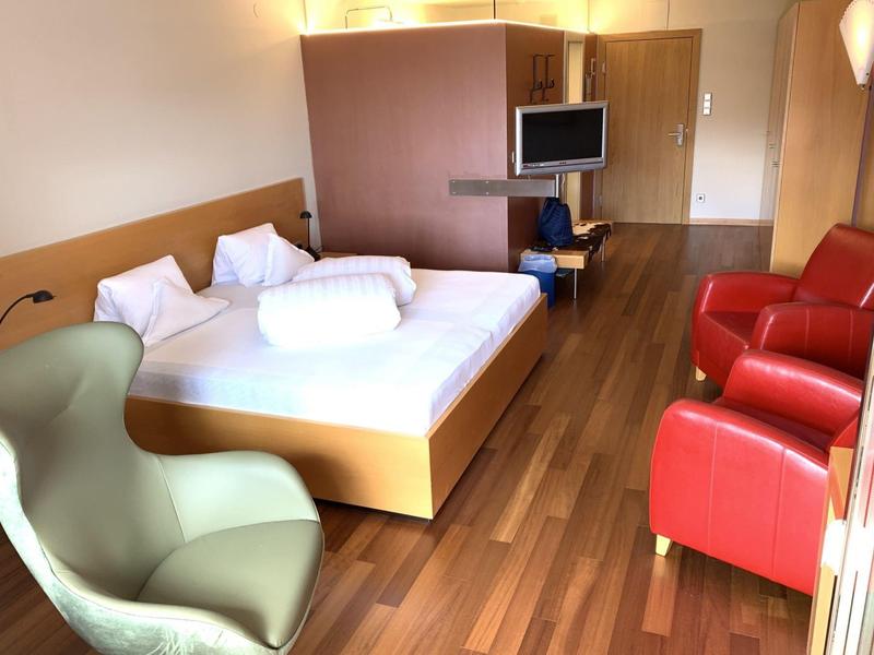 Gemütliches Hotelzimmer mit Doppelbett, zwei roten Sesseln, grünem Sessel und Holzfußboden.