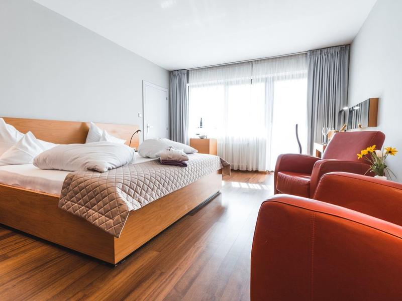 Helles Schlafzimmer mit Holzboden, zwei roten Sesseln und großem Doppelbett mit weißer Bettwäsche.