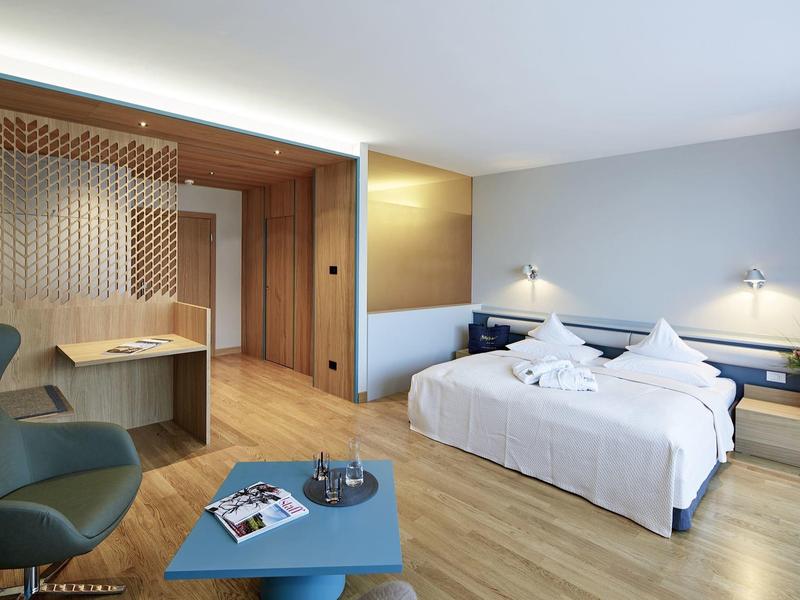 Modernes Hotelzimmer mit Doppelbett, Holzmöbeln, blauer Bank und stilvoller Beleuchtung.