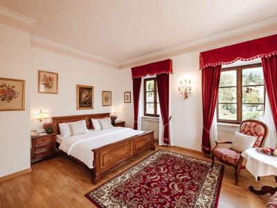 Gemütliches Schlafzimmer mit Holzmöbeln, roten Vorhängen und Teppich vor zwei Fenstern.