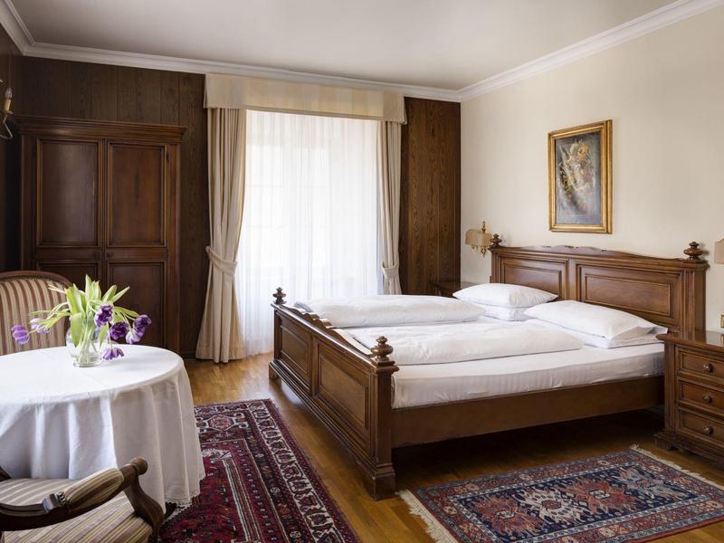 Gemütliches Schlafzimmer mit Holzmöbeln, Teppichen, Tisch mit Blumen und hellem Fensterlicht.